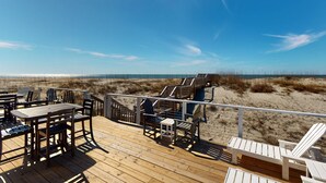 Une terrasse en bois avec des sièges extérieurs, donnant sur une plage bordée de dunes de sable.