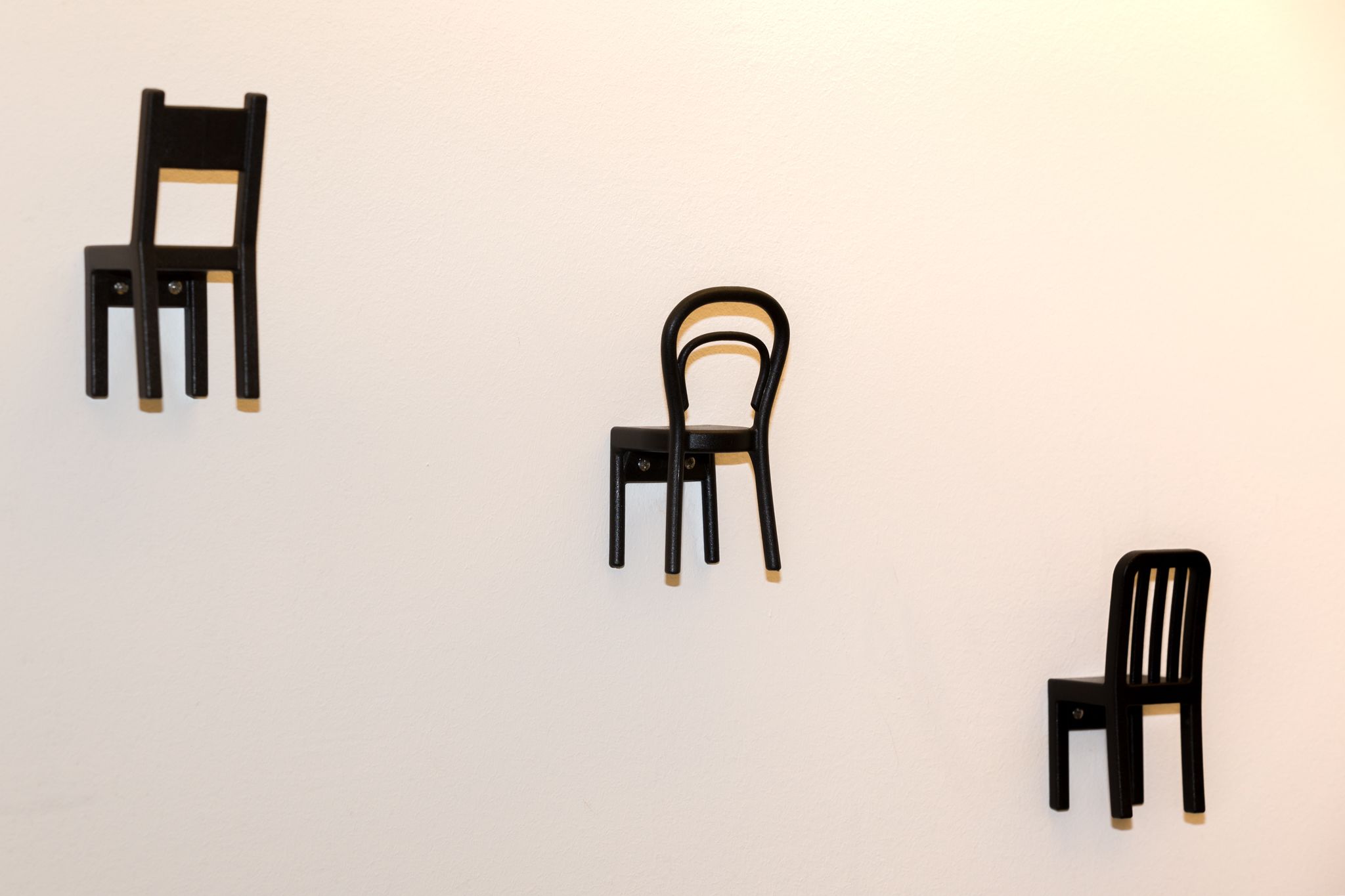 Drie zwarte stoelen voor een effen muur.
