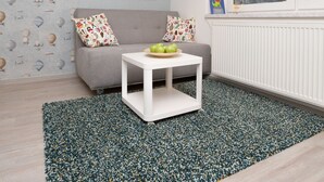 A modern living room with a grey sofa, colorful pillows, a white coffee table with apples, a patterned rug, and a large abstract painting on the wall. - Big Yard (Ljubljana)