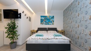 A modern bedroom with a large bed, a flat-screen TV, a potted plant, and a wall with a pattern of hot air balloons. - Big Yard (Ljubljana)