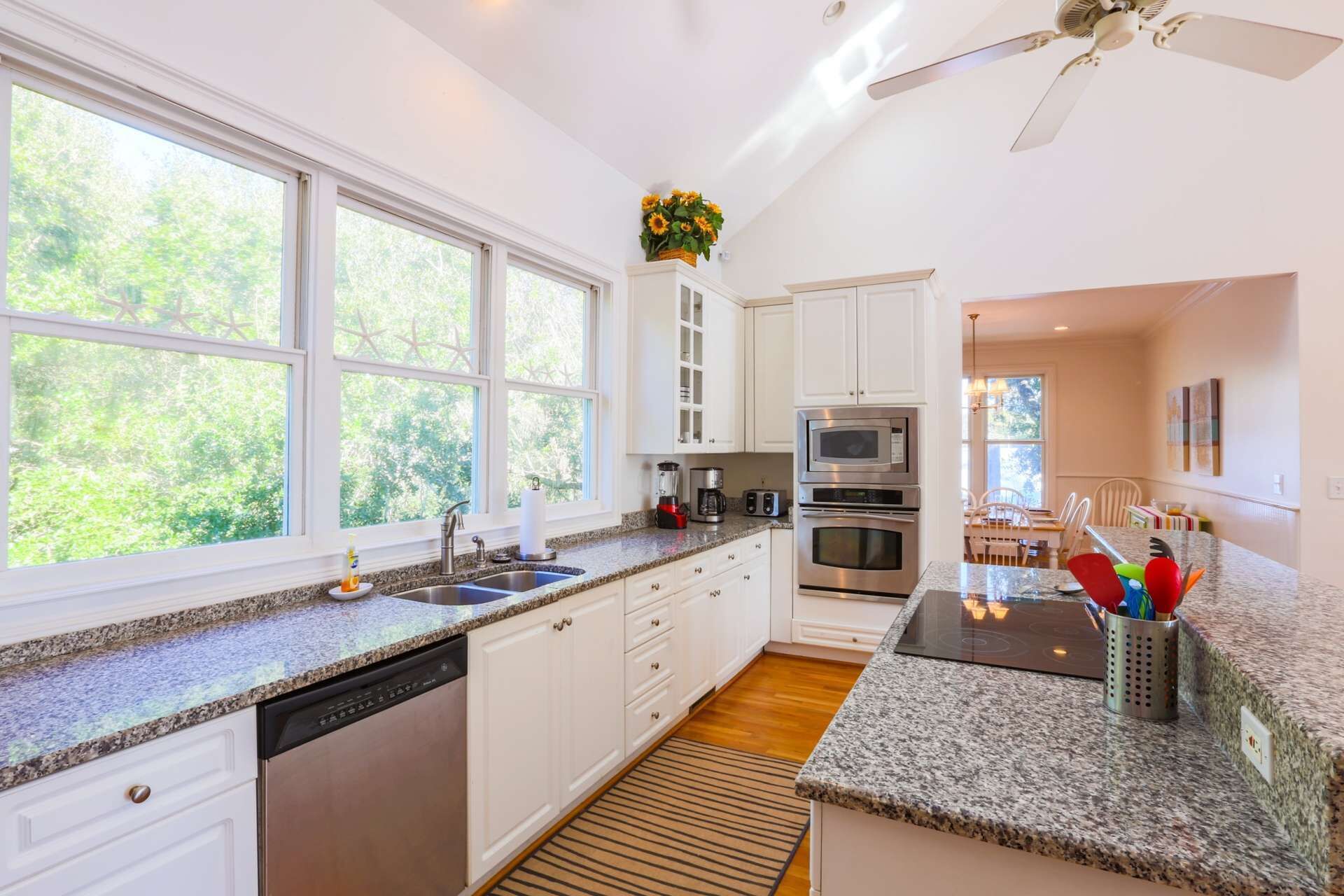 A modern kitchen with white cabinets, granite countertops, a dishwasher, a stove, and a ceiling fan.