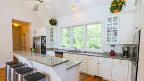 A modern kitchen with white cabinets, granite countertops, a large window, and a bar area with stools.