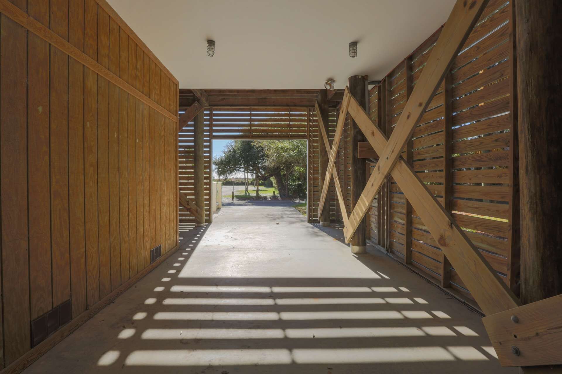 A corridor with wooden walls and a sloped ceiling, leading to an outdoor area with trees.