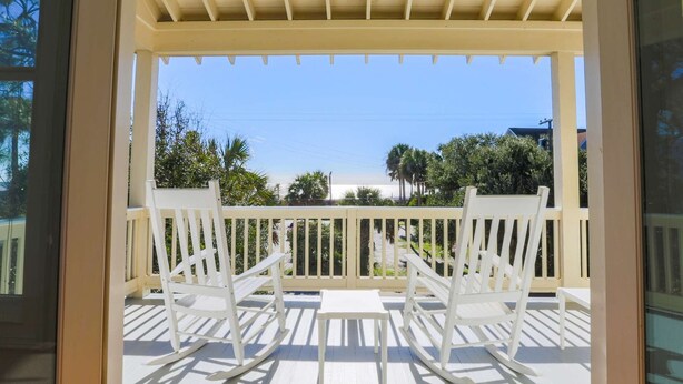 A covered porch with two rocking chairs and a view of the beach.