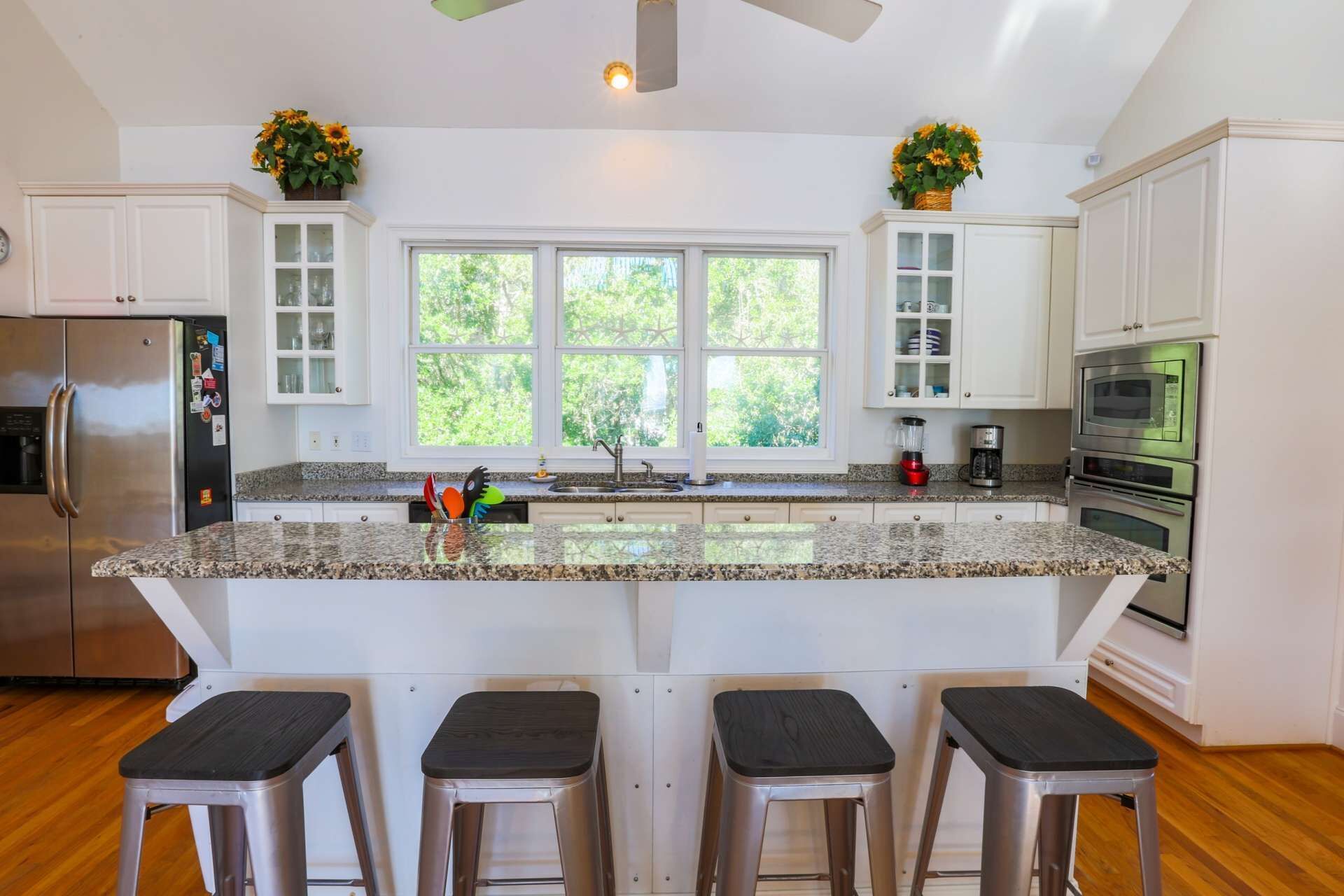 A modern kitchen with white cabinetry, granite countertops, a central island with bar stools, a refrigerator, an oven, and a microwave.