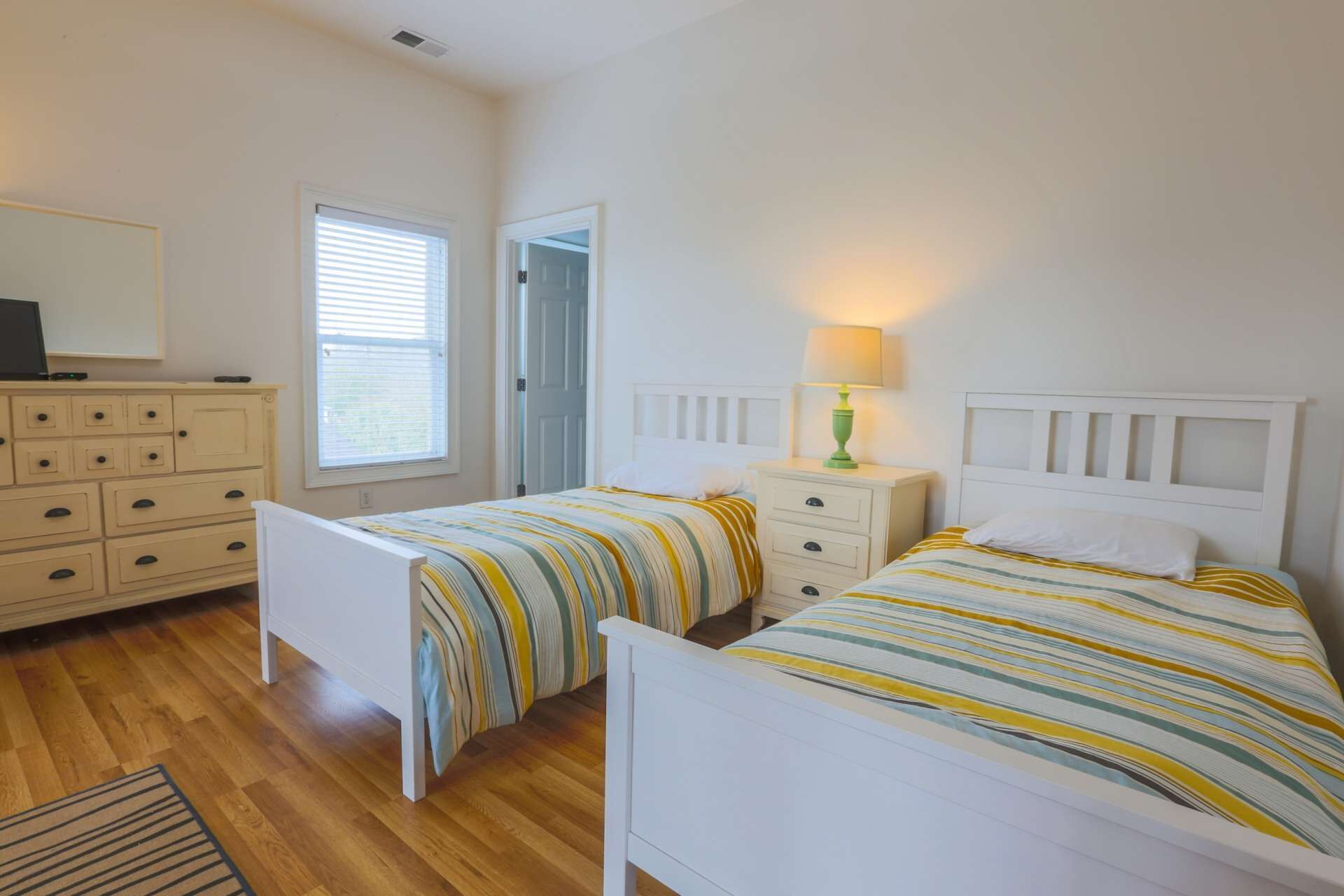 A bedroom with two single beds, a dresser, a lamp, and a television on a dresser.