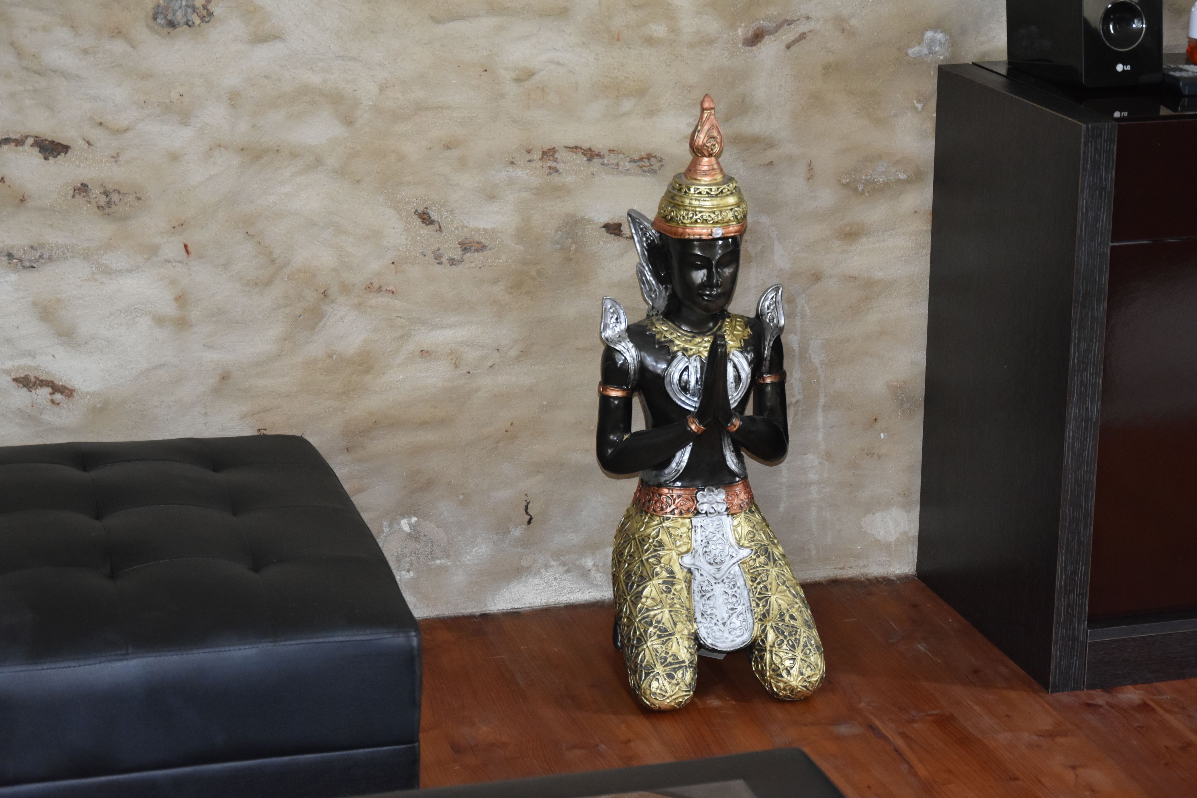 Eine Statue einer Gottheit mit mehreren Armen, sitzend auf einem Holzboden vor einer strukturierten Wand.