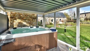 Un jacuzzi bajo un porche cubierto, con paredes de piedra y vista a un edificio de piedra.