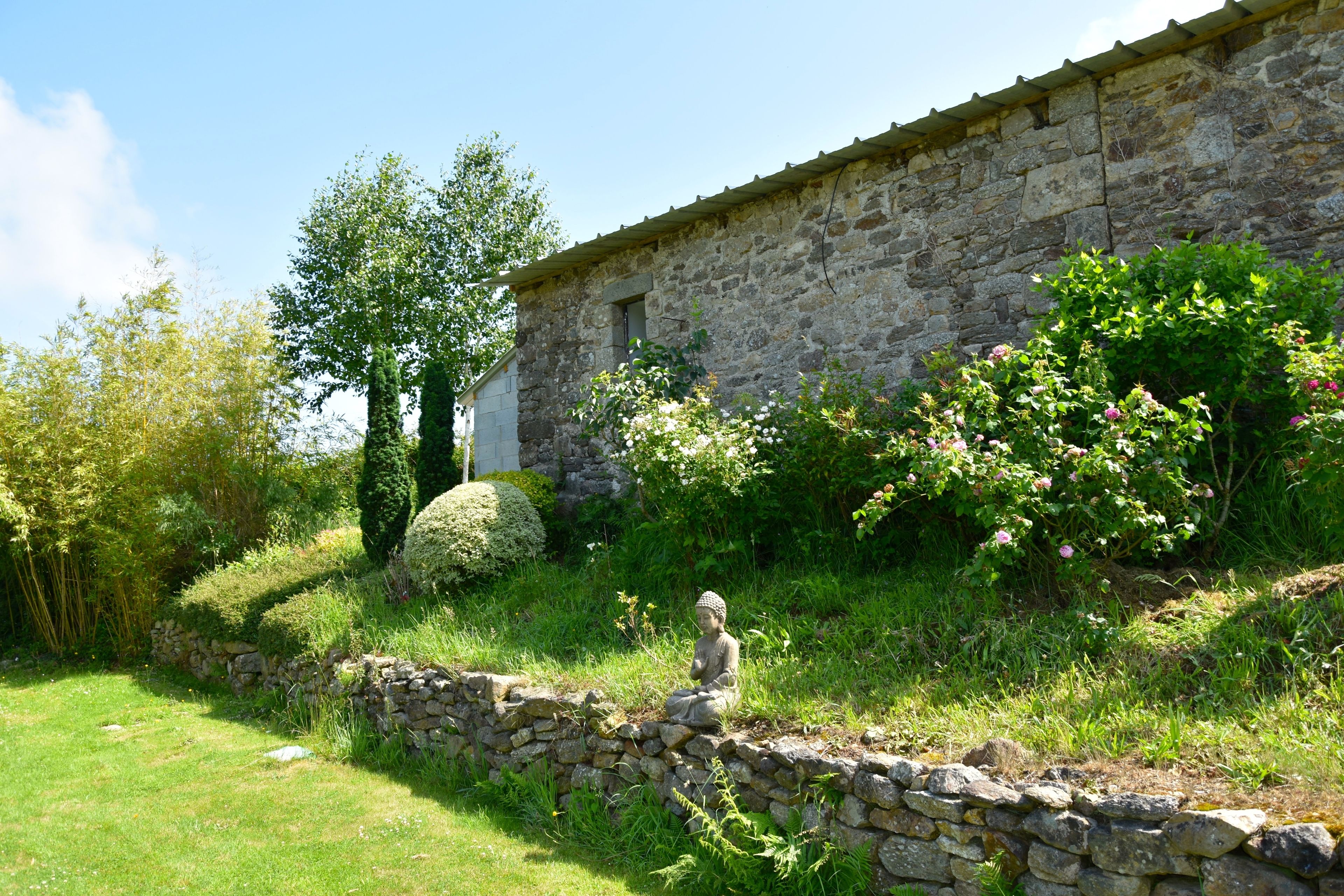 A stone building with a rustic stone wall and a Buddha statue in a garden.