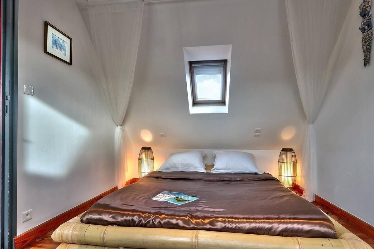 Une chambre à coucher avec un lit, une fenêtre, deux lampes de chevet et un petit tableau accroché au mur.