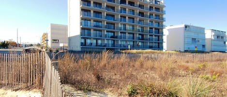 Un hotel de varios pisos con balcones y una playa arenosa al frente.