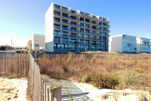 A multi-story hotel with balconies and a sandy beach in the foreground. - XPLORIE ACTIVITIES & LINENS INCLUDED*! OUTDOOR POOL (IN SEASON), TENNIS & MORE!!! (Ocean City)