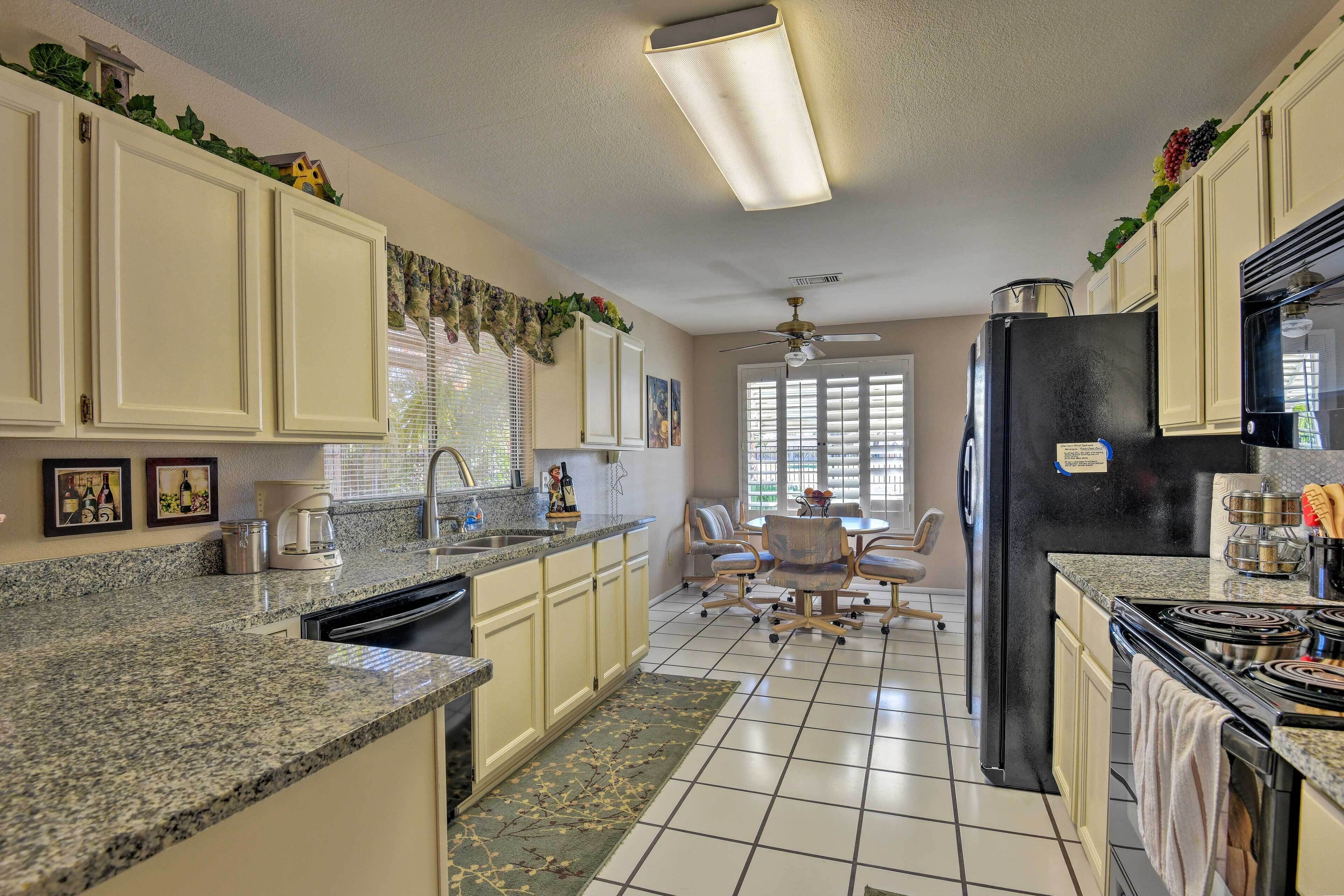 A kitchen with granite countertops, a black refrigerator, and a dining area with a table and chairs.