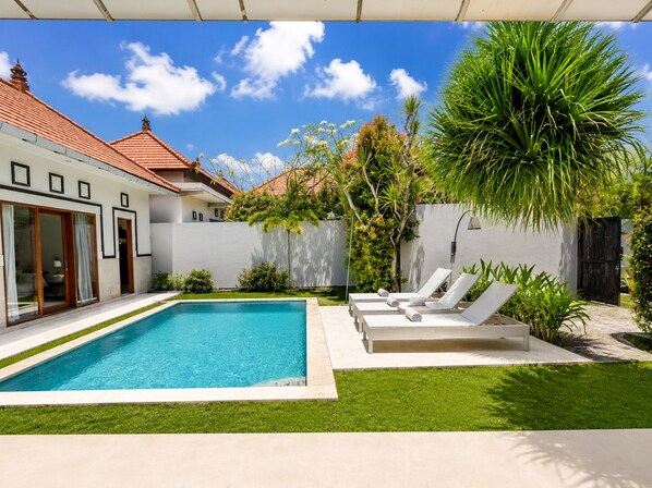 A modern pool area with a clear blue pool, surrounded by a well-maintained lawn and a variety of tropical plants. - 3 Bedrooms Central Seminyak (Seminyak)