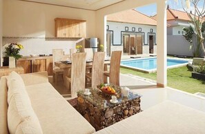A modern living room with a glass coffee table, a sofa, and a dining area with wooden chairs. - 3 Bedrooms Central Seminyak (Seminyak)