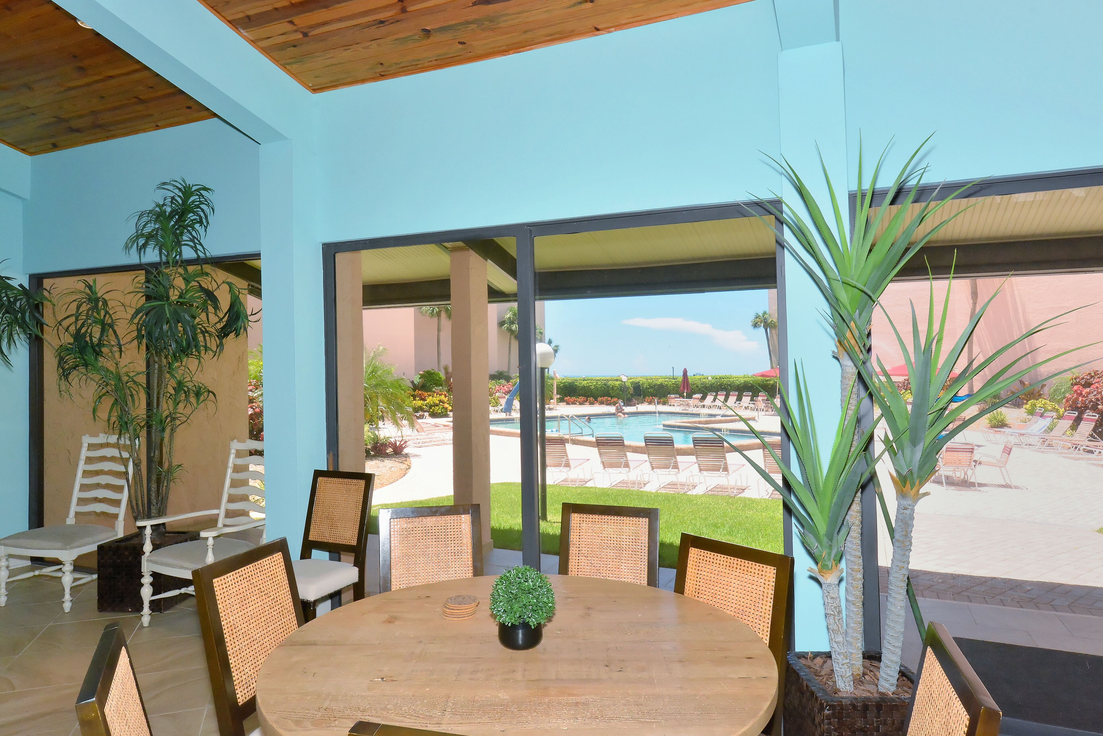 A dining area with a round table and chairs, large windows overlooking a pool and outdoor seating area.