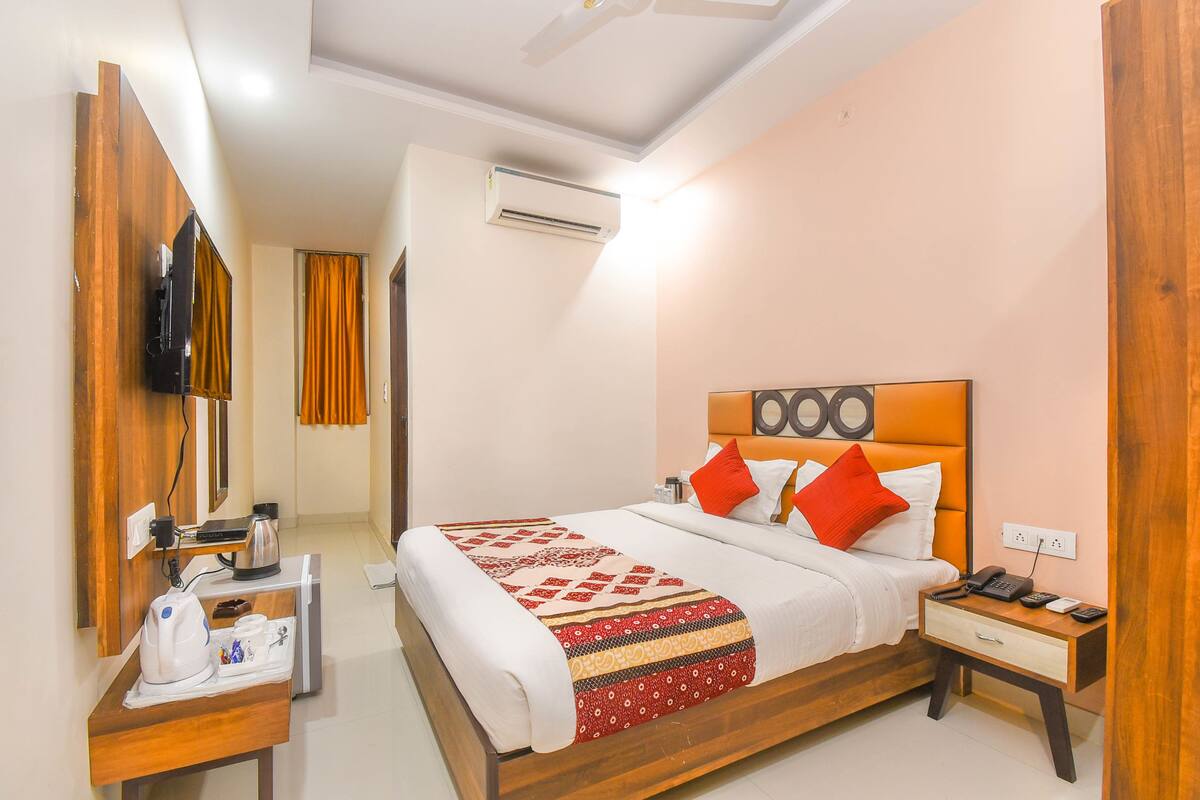 A hotel room with a bed, bedside table, and a desk with a coffee maker and cups.