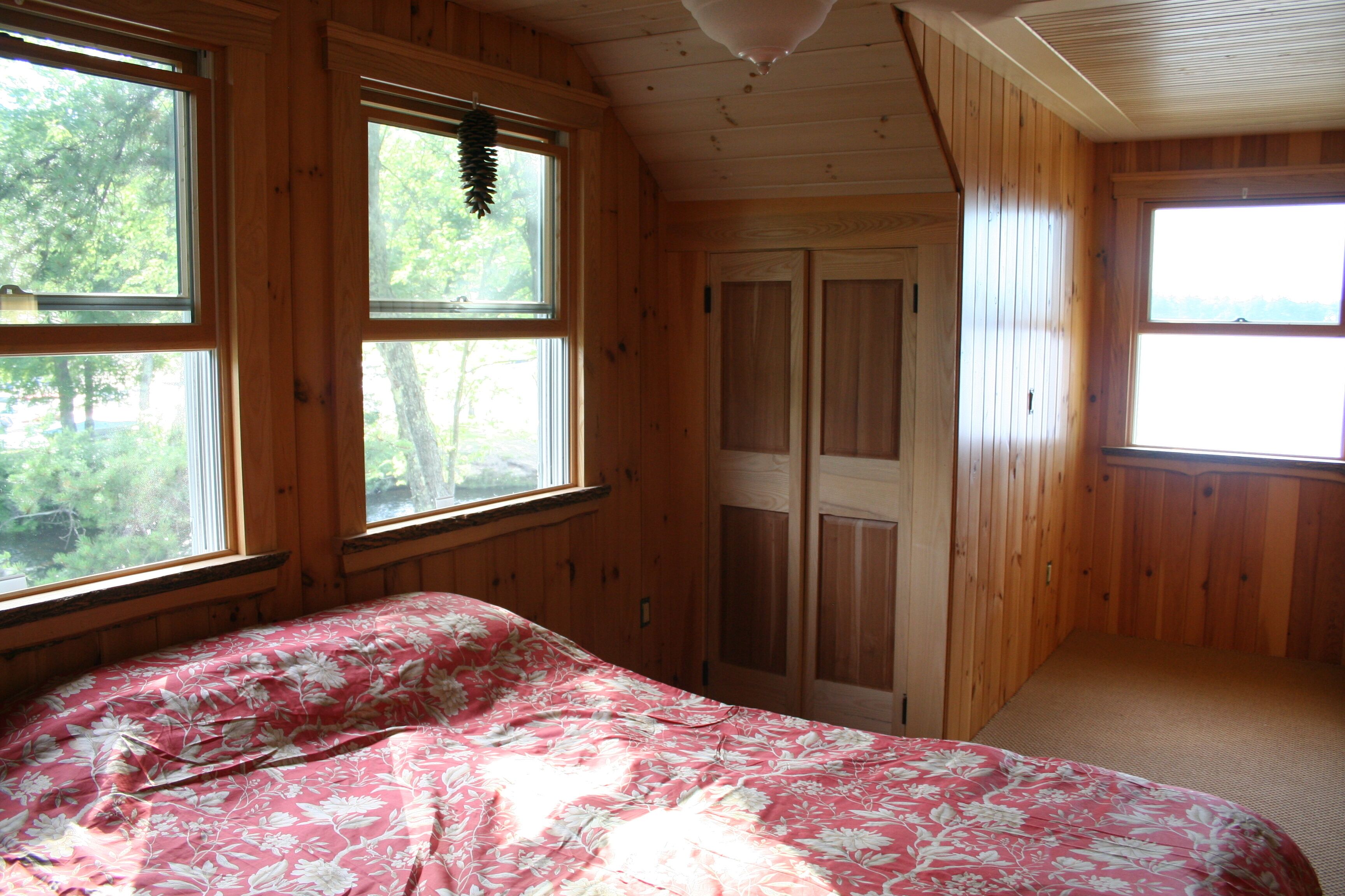 A bedroom with a bed, wooden walls, and large windows.
