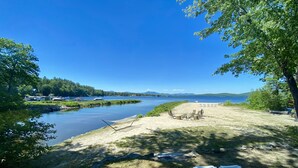 A lakeside view with a sandy beach, lounge chairs, and a small table. - Booking for next summer. (Center Ossipee)