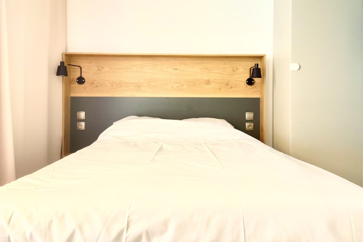 A bed with a wooden headboard, two wall-mounted lamps, and a plain wall.