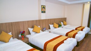 Habitación de hotel con cuatro camas individuales, cada una con sábanas blancas y colchas a rayas anaranjadas y marrones. Hay una pequeña mesa con un florero y una botella de agua.