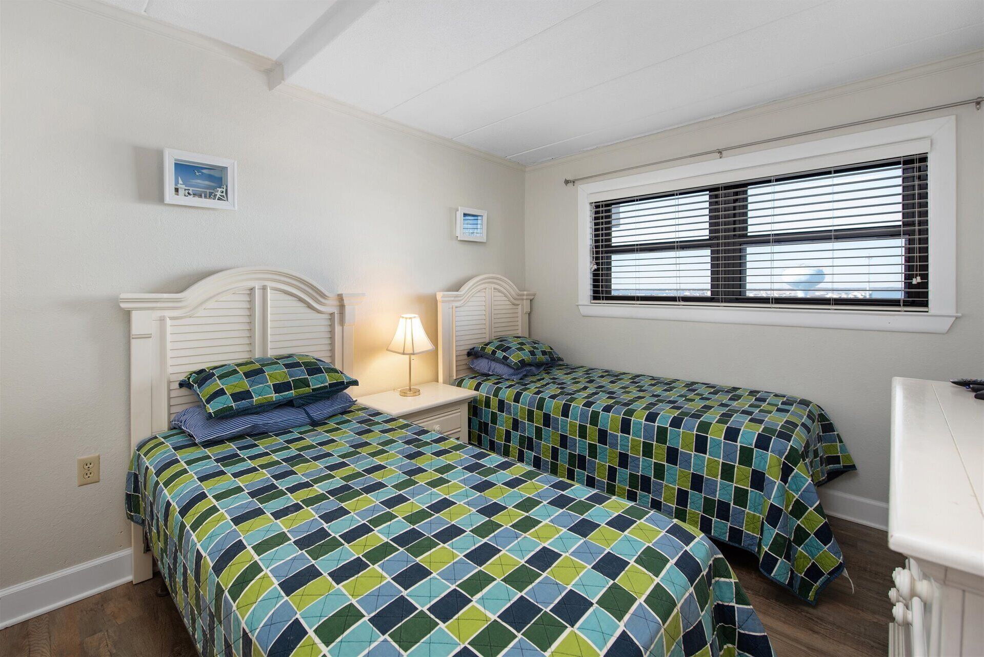 Une chambre à coucher avec deux lits, chacun recouvert d’une couvre-lit à motifs, une lampe de chevet et une fenêtre avec des stores.