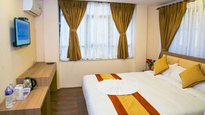 Una habitación de hotel con cama, escritorio con hervidor, televisión y ventana con cortinas.