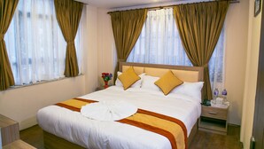 Habitación de hotel con una cama grande, una mesita de noche, una ventana con cortinas e iluminación en el techo.