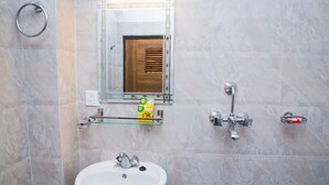 Un baño con un lavamanos blanco, un estante de vidrio con artículos de tocador, un tozalengua y una ducha con cabezal de ducha de mano.
