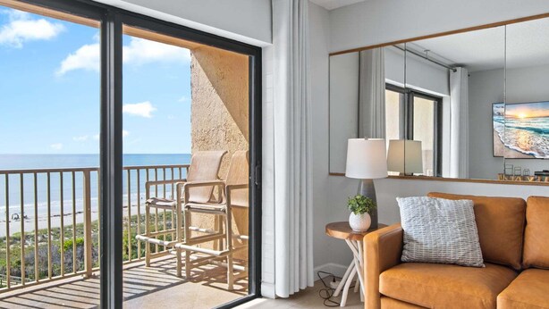 A balcony with chairs, a sofa, a lamp, and a painting of a beach scene.