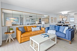 Een moderne woonkamer met een grote spiegel, twee banken, een salontafel en een keuken op de achtergrond.