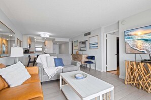 A modern living room with a sofa, coffee table, and a TV on a wall. - Top-Floor Penthouse + Direct Ocean Front Condo! | Spacious 3-Bedroom is Ideal for Families & Groups! (Cape Canaveral)