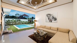 A modern living room with a beige sofa, a coffee table, and a painting on the wall. A pool is visible through the glass door. - 3Bedrooms Central Seminyak walking distance to the Boutique shop,Restaurant,Bar (Seminyak)