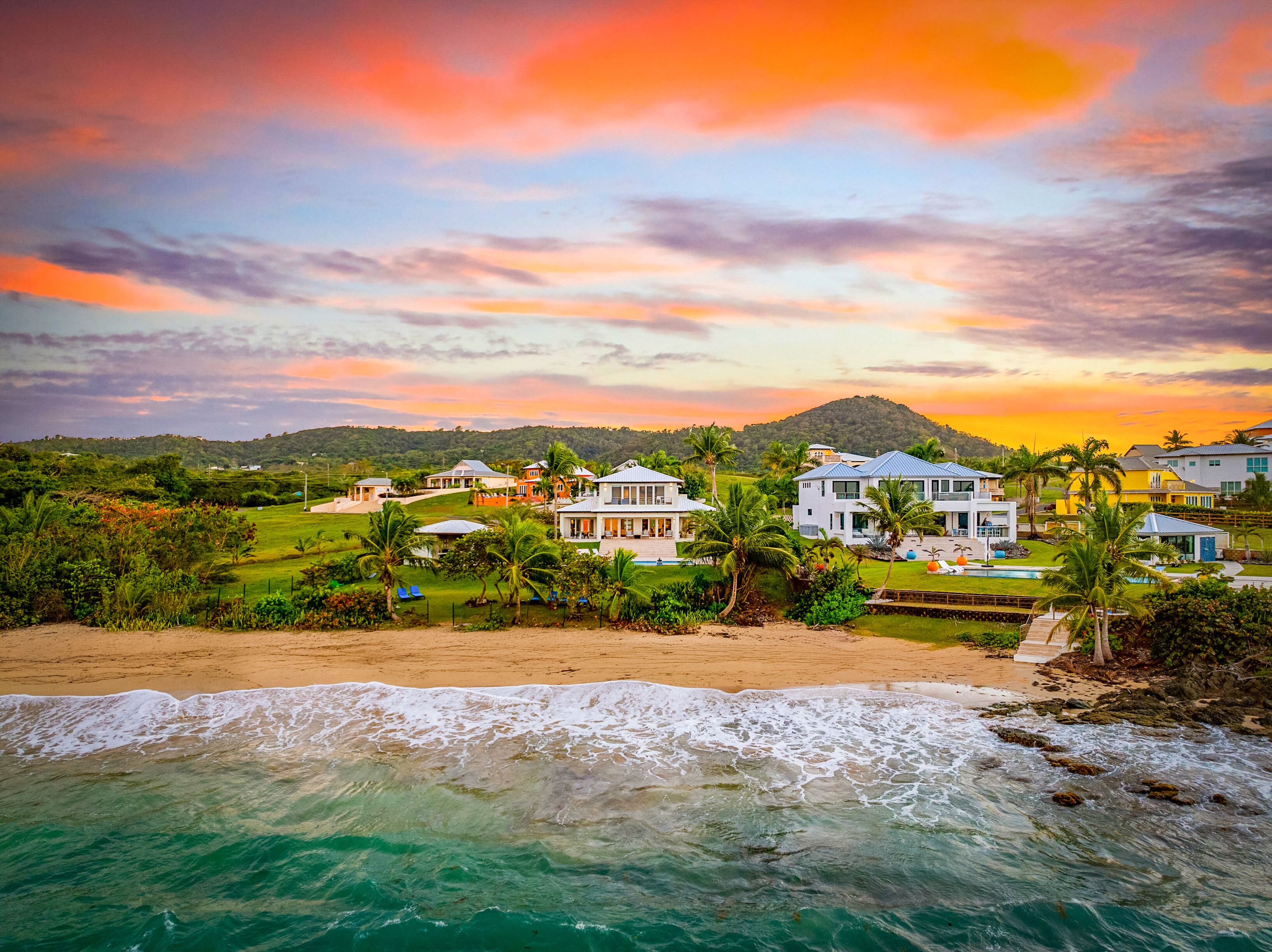 A beachfront property with multiple houses, a swimming pool, and a view of the ocean.