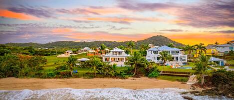 A beachfront property with multiple houses, a swimming pool, and a view of the ocean.