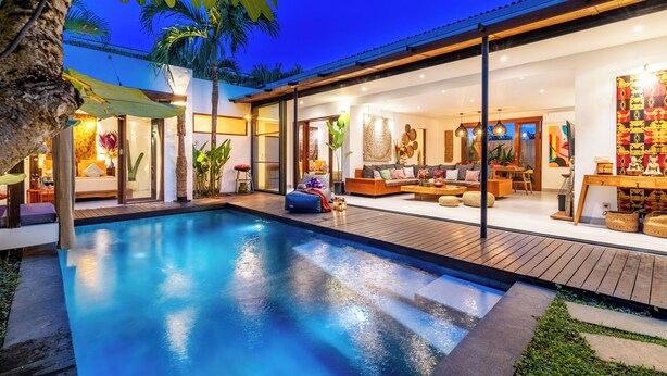 A modern house with a swimming pool, wooden deck, and a well-lit interior.