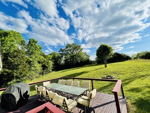Una terraza al aire libre con una mesa y sillas, rodeada de un paisaje cubierto de césped y árboles.