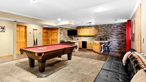 A spacious living area with a pool table, a sofa, a kitchen with wooden cabinets, and a stone accent wall. - BEAUTIFUL VERY SPACIOUS home in heart of Branson - Hot Tub, Game Room,Large Yard (Branson)