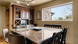 A dining area with a glass-top table, wooden cabinets, and a large window with a view of the outside. - BEAUTIFUL VERY SPACIOUS home in heart of Branson - Hot Tub, Game Room,Large Yard (Branson)
