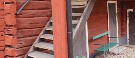 Una escalera de madera que sube a un porche con barandilla metálica.