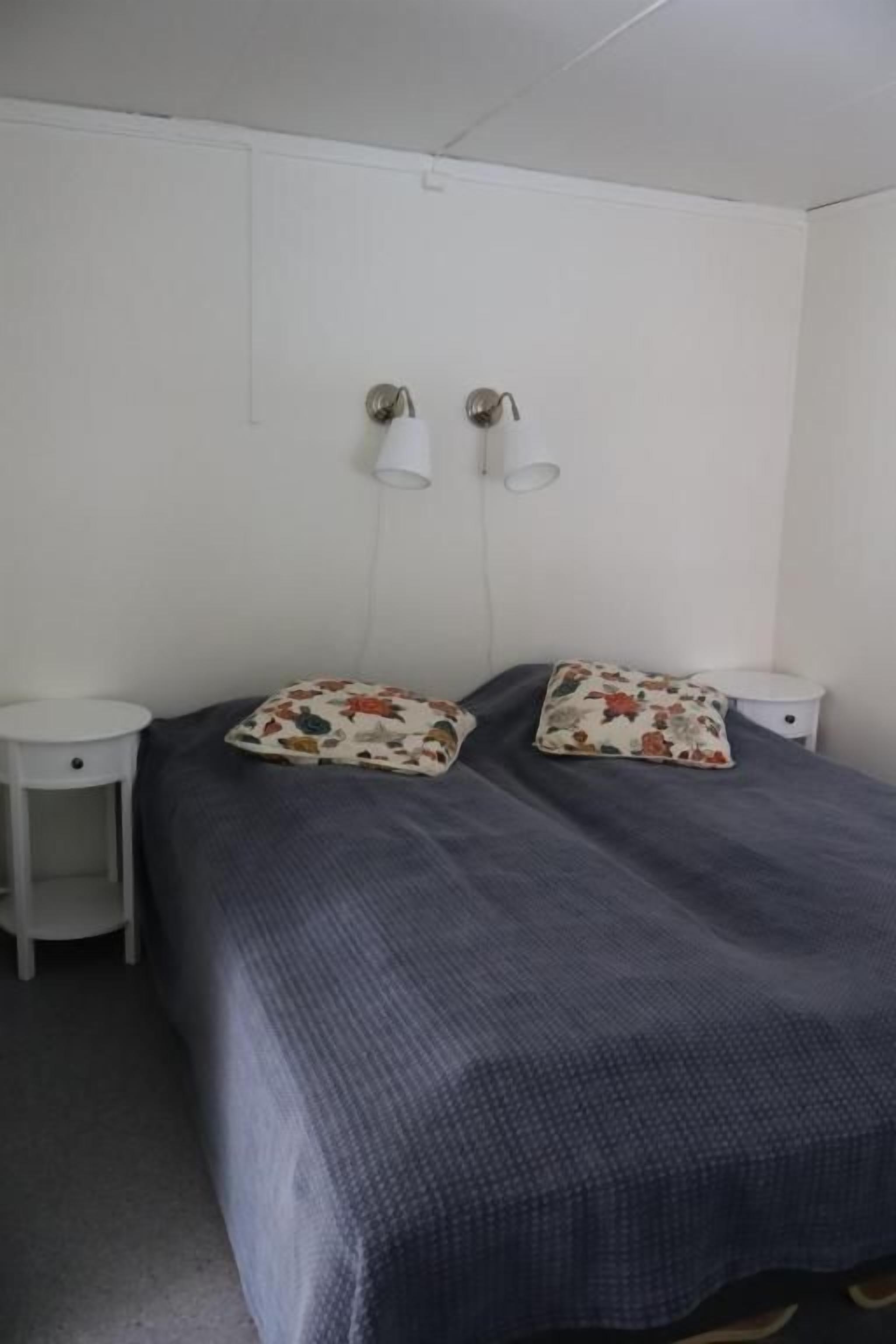 Une chambre avec un lit simple, une table de chevet, une lampe et un luminaire fixé au mur.