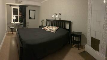 A bedroom with a large bed, a bedside table, a nightstand, a mirror, a lamp, and a small table with a chair.