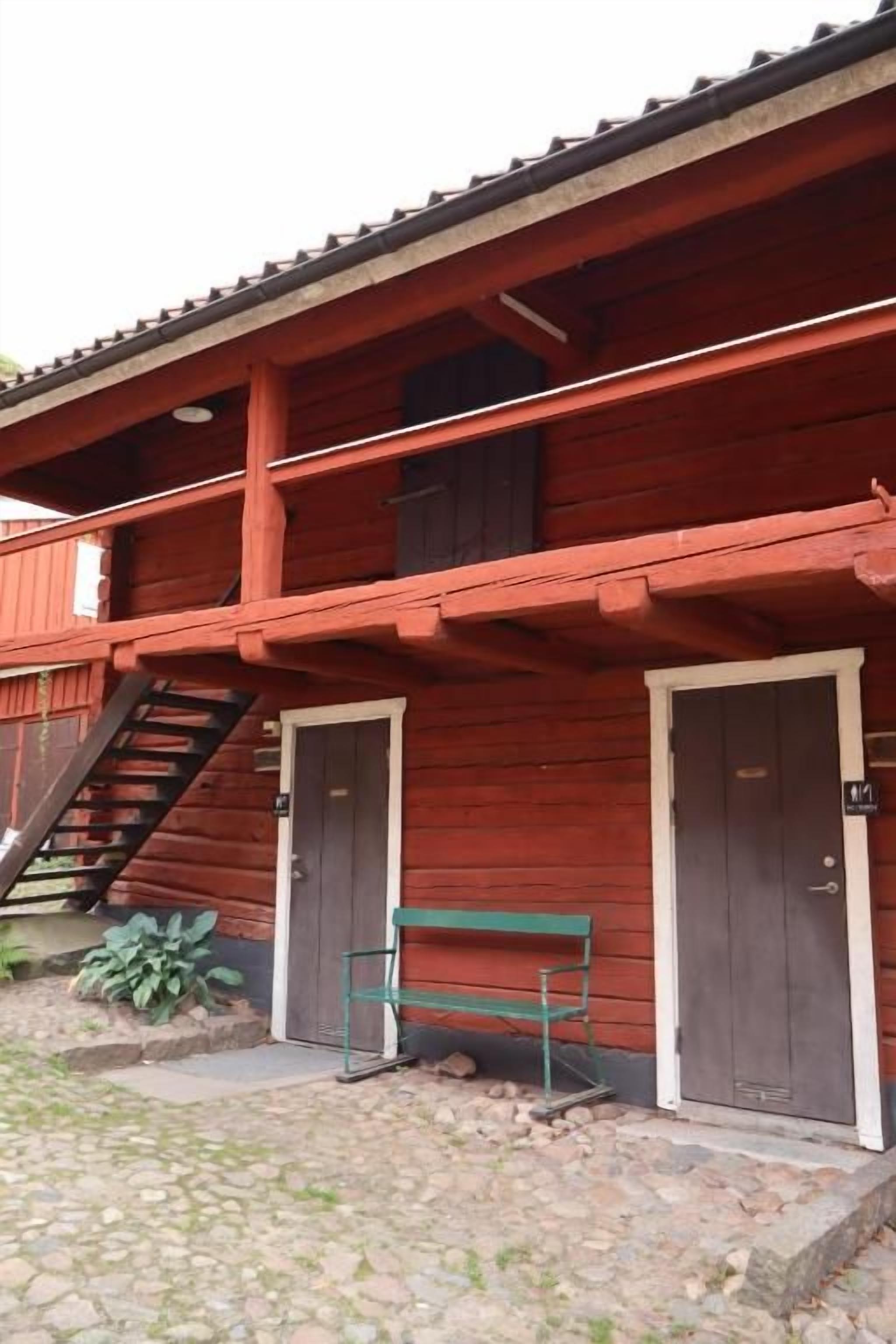 A red wooden building with a balcony, a bench, and a staircase leading to an upper level.