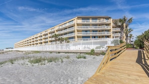 Um hotel à beira-mar com várias varandas, um calçadão de madeira e uma área de praia arenosa.