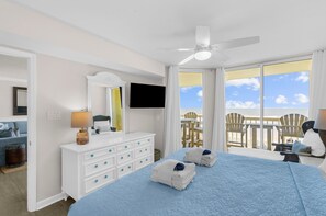 Habitación de hotel con cama, cómoda, televisor, balcón con sillas y ventilador de techo.