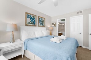 Una camera d'hotel con un letto, due lampade a parete, un comodino, una porta bianca e un bagno visibile attraverso una porta aperta.