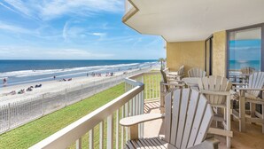 Varanda com vista para a praia e oceano. Há várias cadeiras Adirondack e uma mesa com cadeiras.
