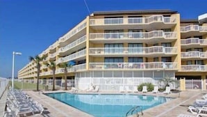 Um hotel de vários andares com varandas, piscina e espreguiçadeiras.