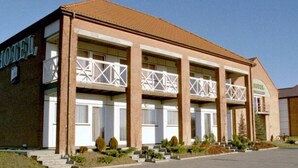 Een hotel met twee verdiepingen, een bakstenen gevel, meerdere balkons en een parkeerplaats.