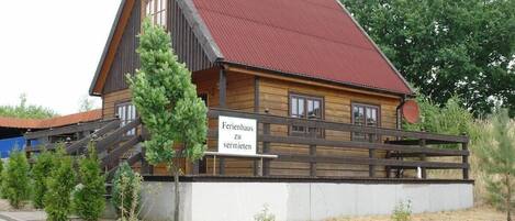 A wooden building with a red roof, a sign reading "Ferienhaus zu vermieten," and a wooden fence.